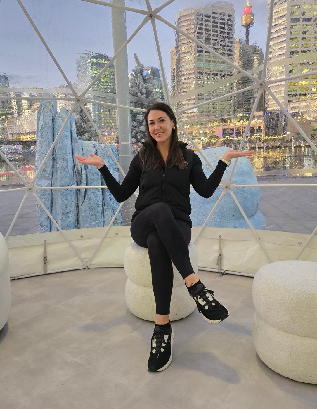 Georgie seated inside a transparent IGLOOZE dome with the Sydney skyline beyond