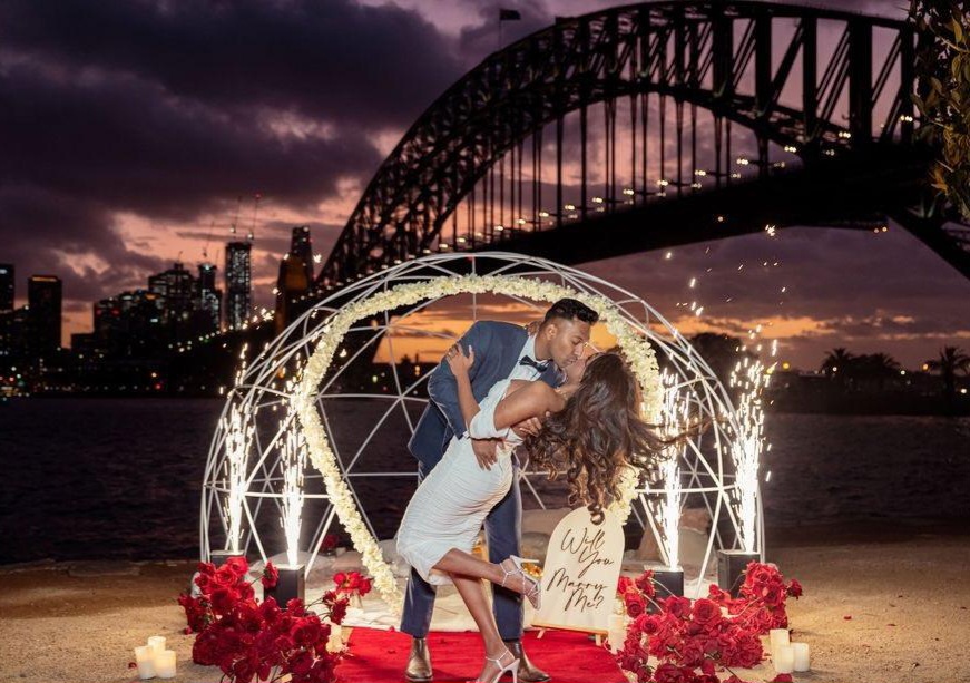 Couple kissing in front of dome with Sydney Harbour Bridge at sunset